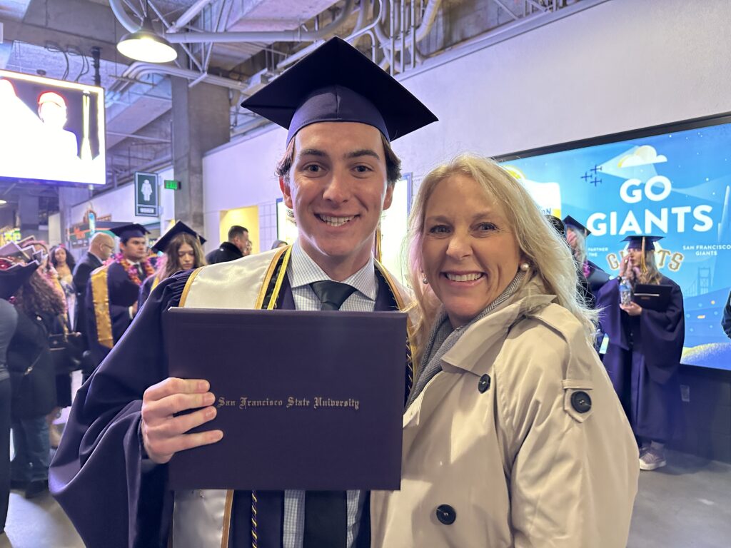 Graduate posing with an older woman while holding a diploma at an indoor celebration.