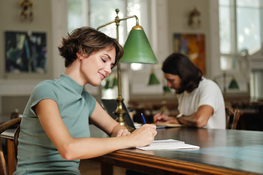 Student writing notes at a table in a quiet library.