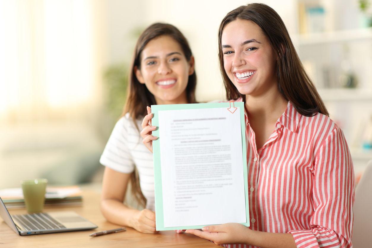 Two students smiling and holding up an acceptance letter or official document.
