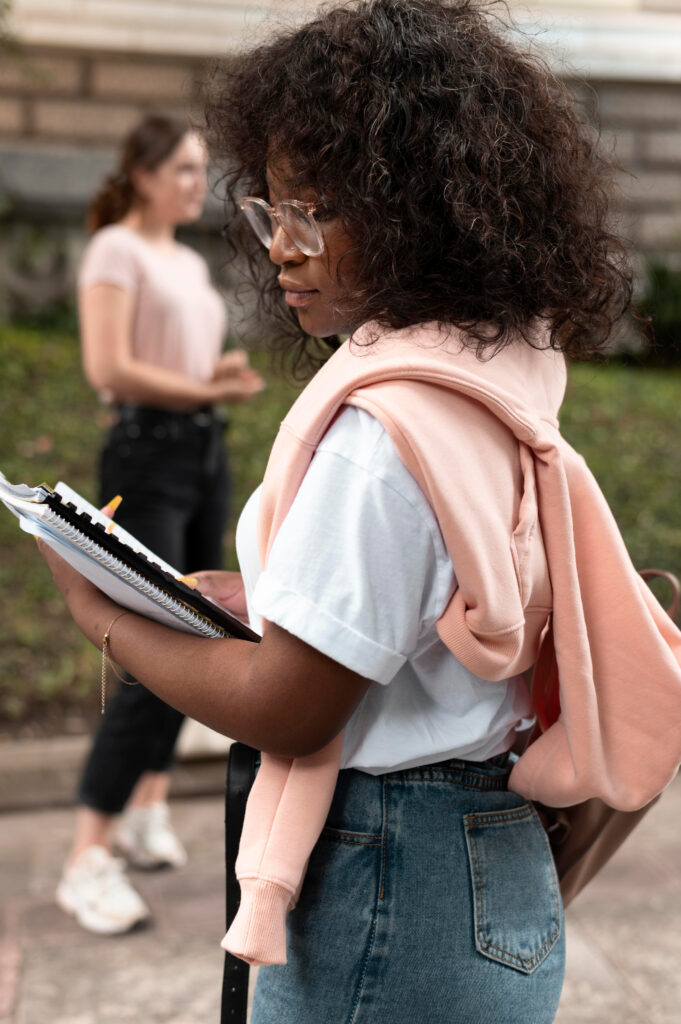 Student with a backpack reading a notebook while walking on campus.