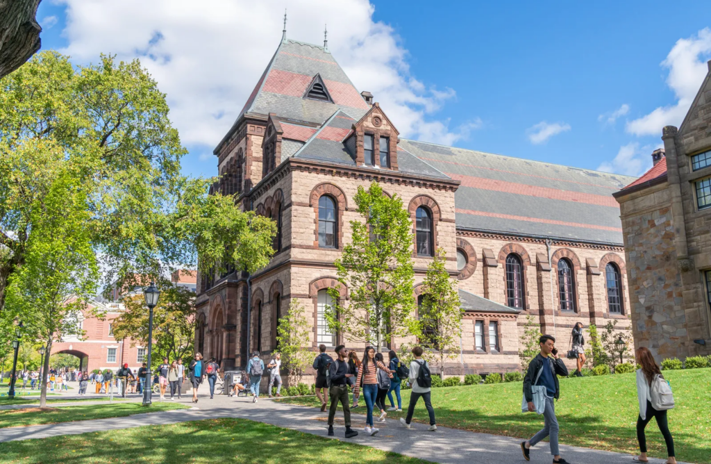 Historic university building with students walking on a path along the green lawn.