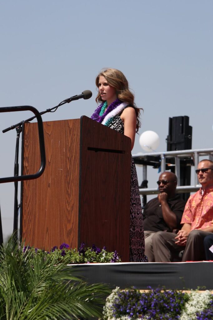Speaker addressing an audience from a podium at an outdoor ceremony.