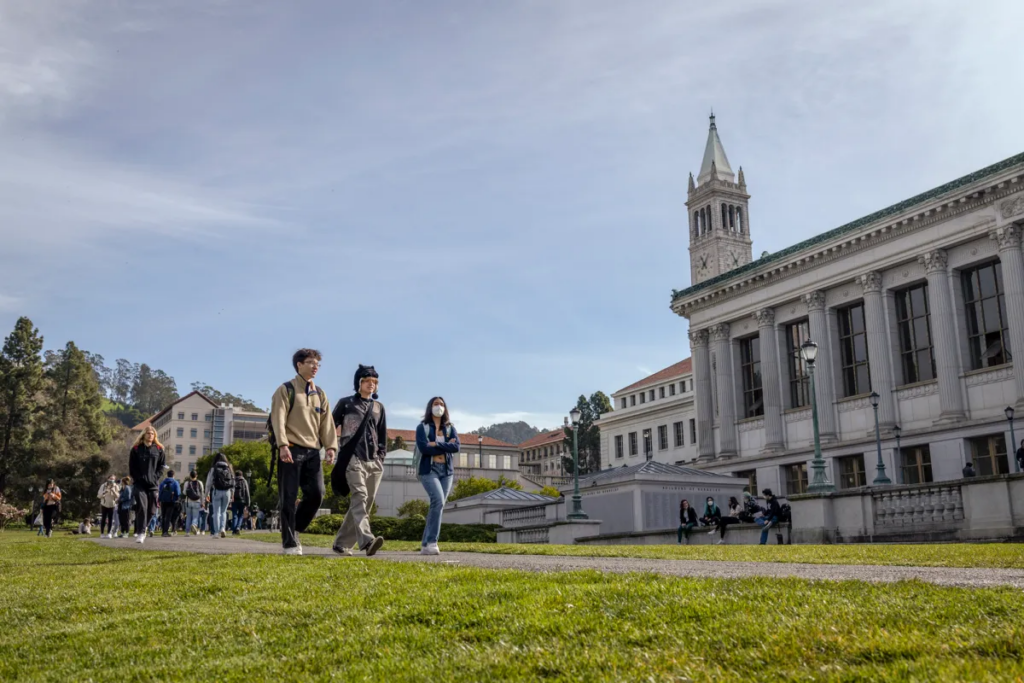 Group of graduates walking across a campus lawn beside a large academic building.