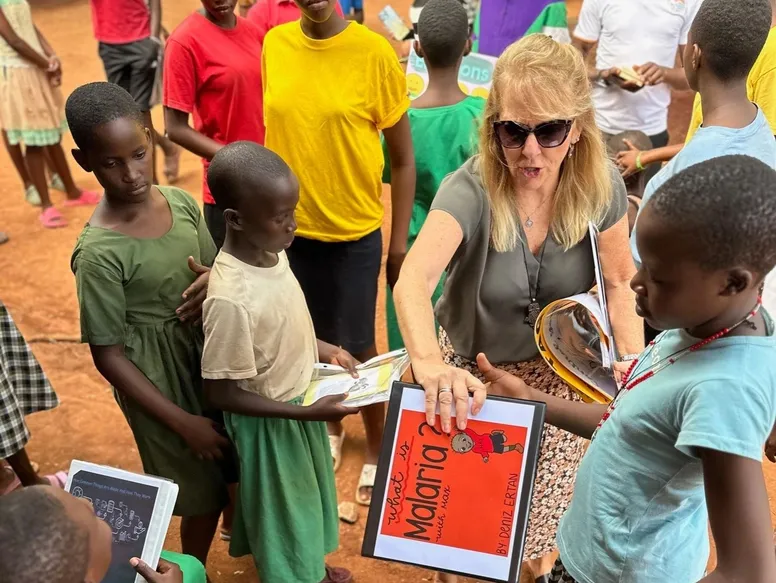Adult showing a book to children gathered around outdoors.
