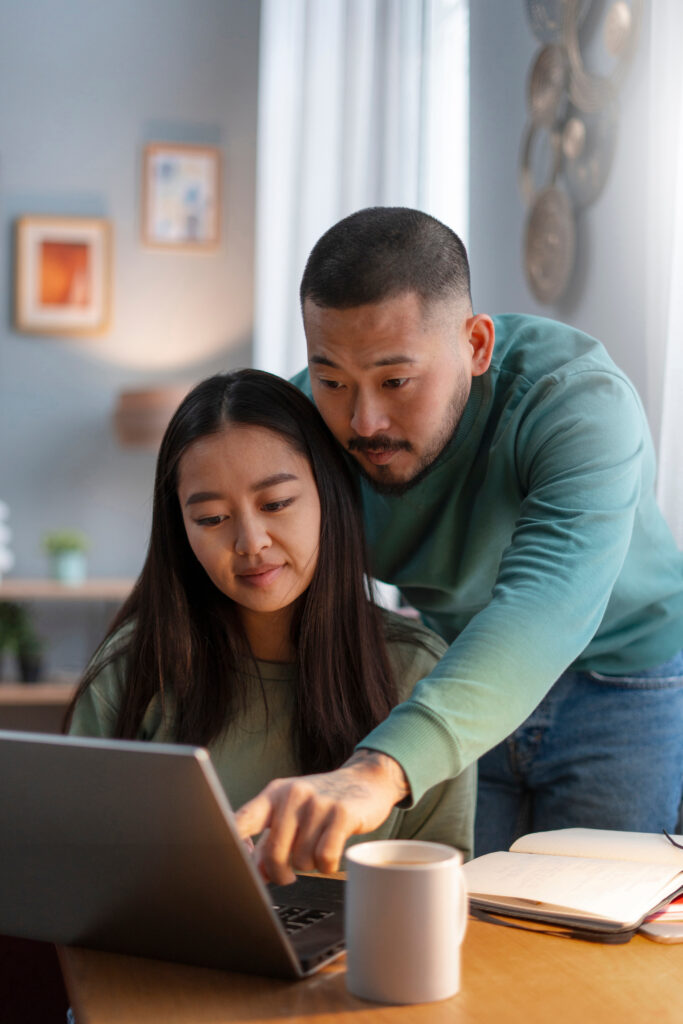 Adult helping a student with homework on a laptop at a kitchen table.