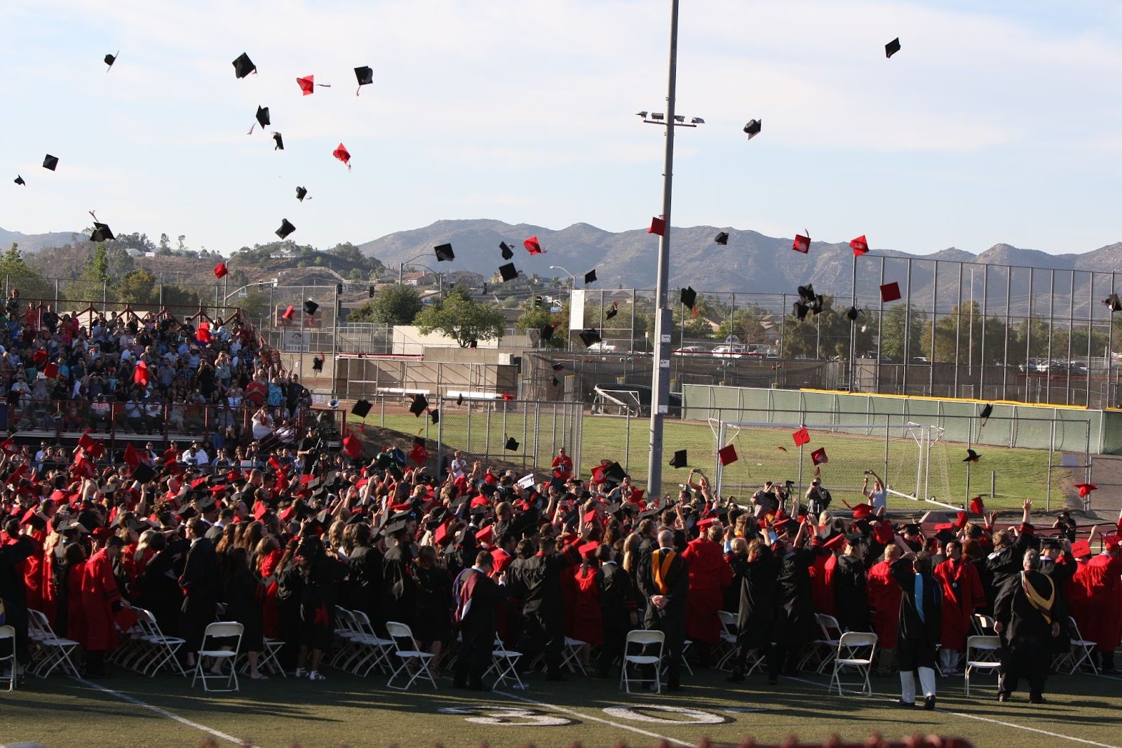 Large outdoor graduation ceremony with a crowd of graduates tossing caps into the air.