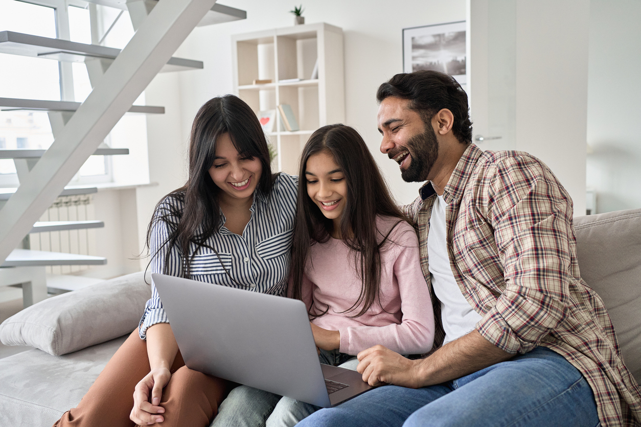 Family sitting together on a couch looking at a laptop at home.