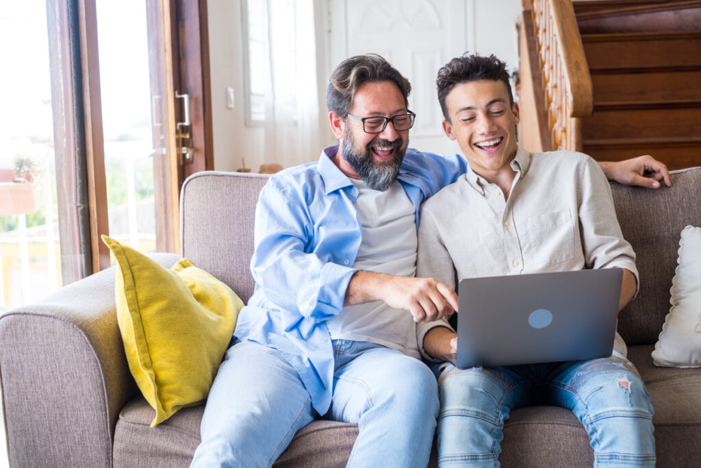 Father and son sitting on a couch using a laptop together.
