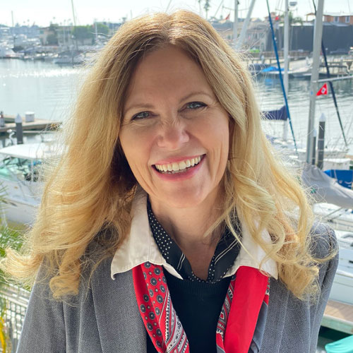 Woman smiling outdoors near boats at a marina.