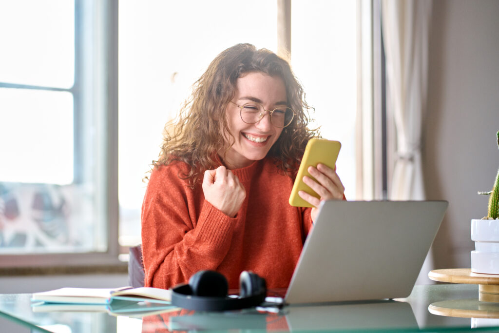 Person working on a laptop at a desk near a bright window.