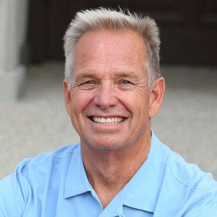 Man in a light blue collared shirt smiling in a close-up portrait.