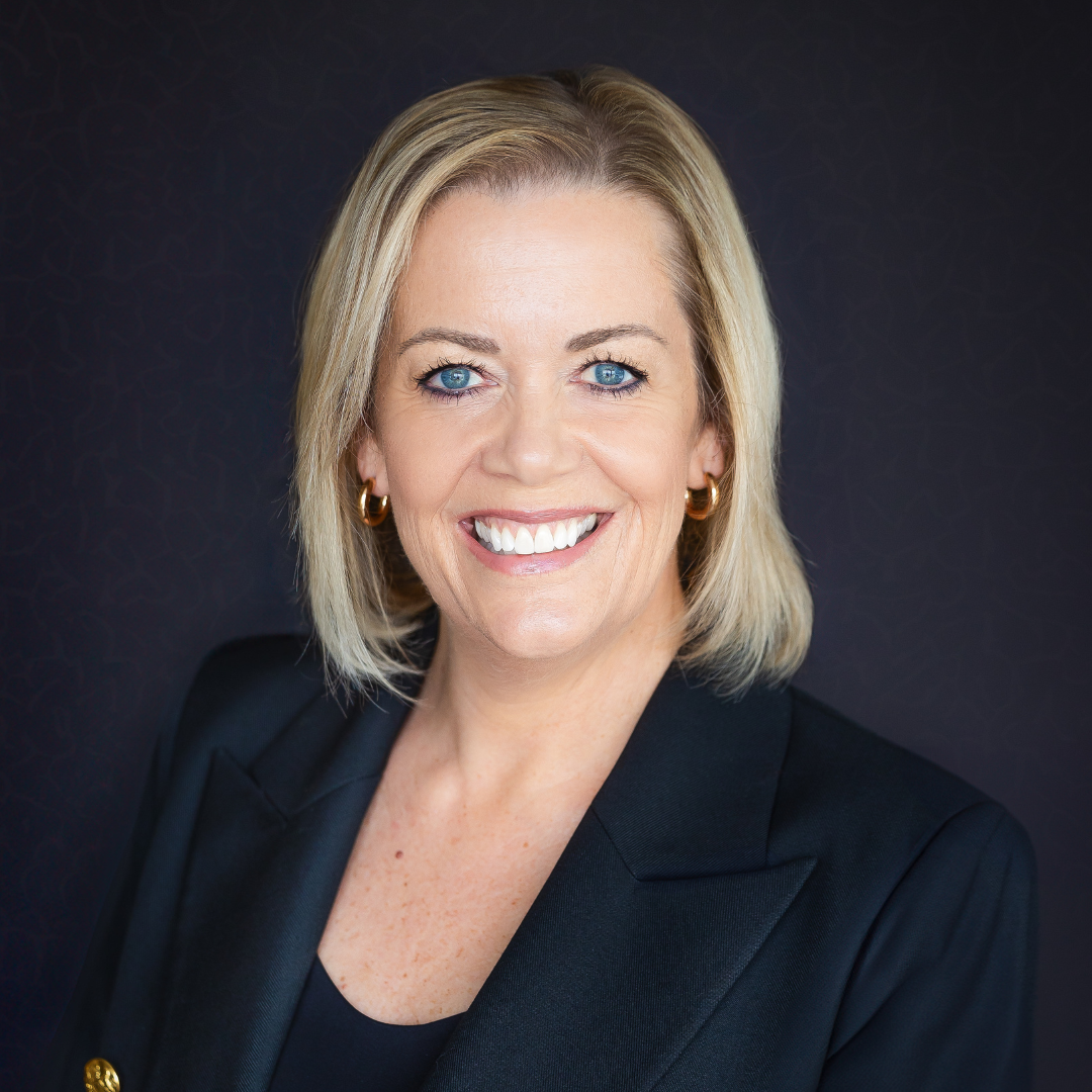 Professional woman in a blazer smiling in a studio headshot.