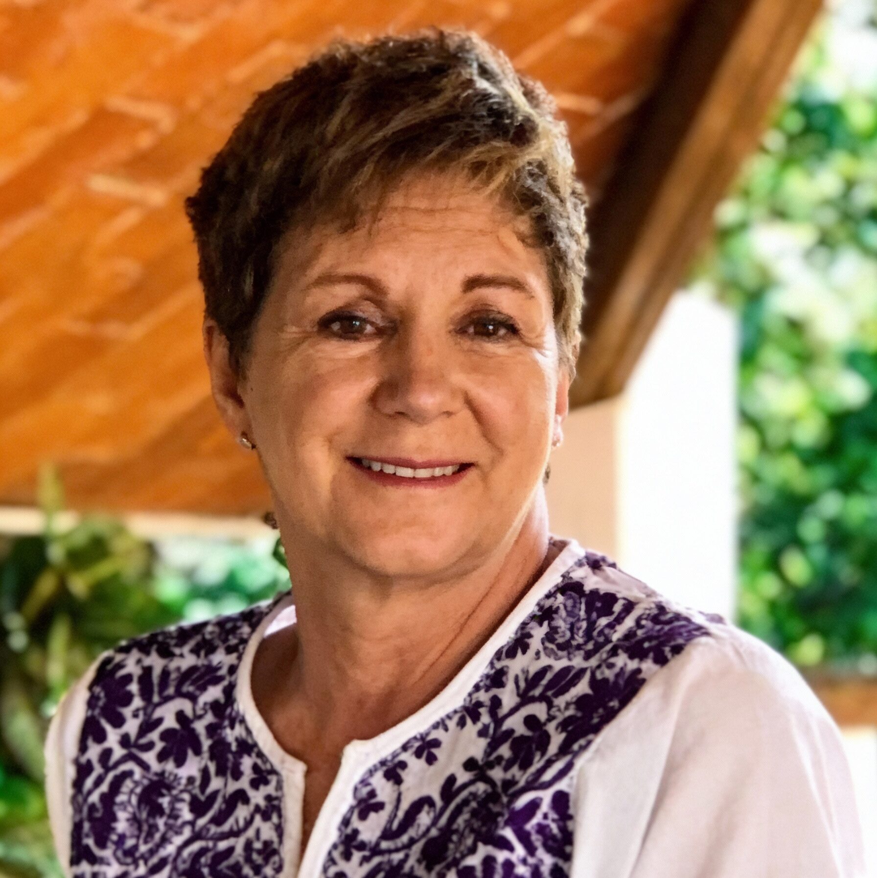 Woman in a patterned vest smiling in a casual outdoor portrait.
