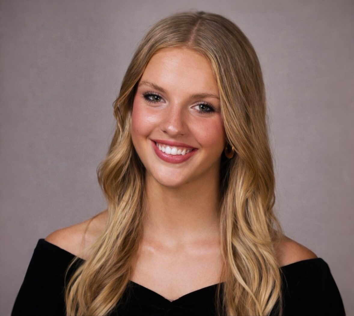 Headshot of a smiling young woman with wavy blonde hair and natural makeup against a neutral background.