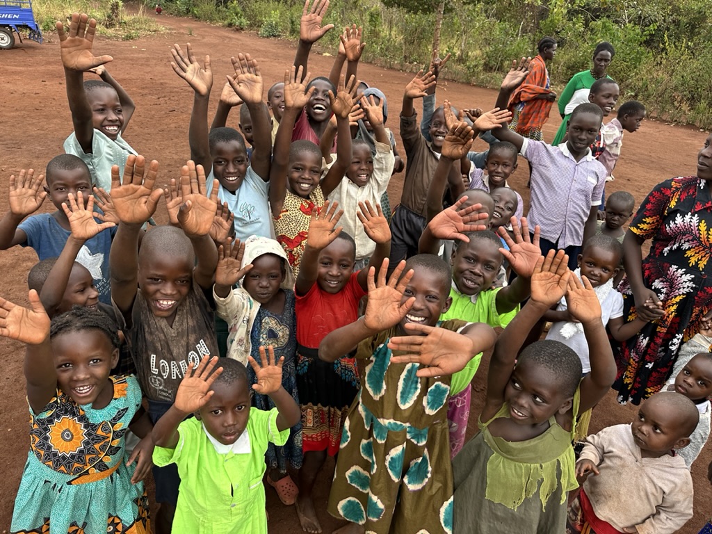 Happy children gathered together waving and smiling on a dirt road in a rural community setting.