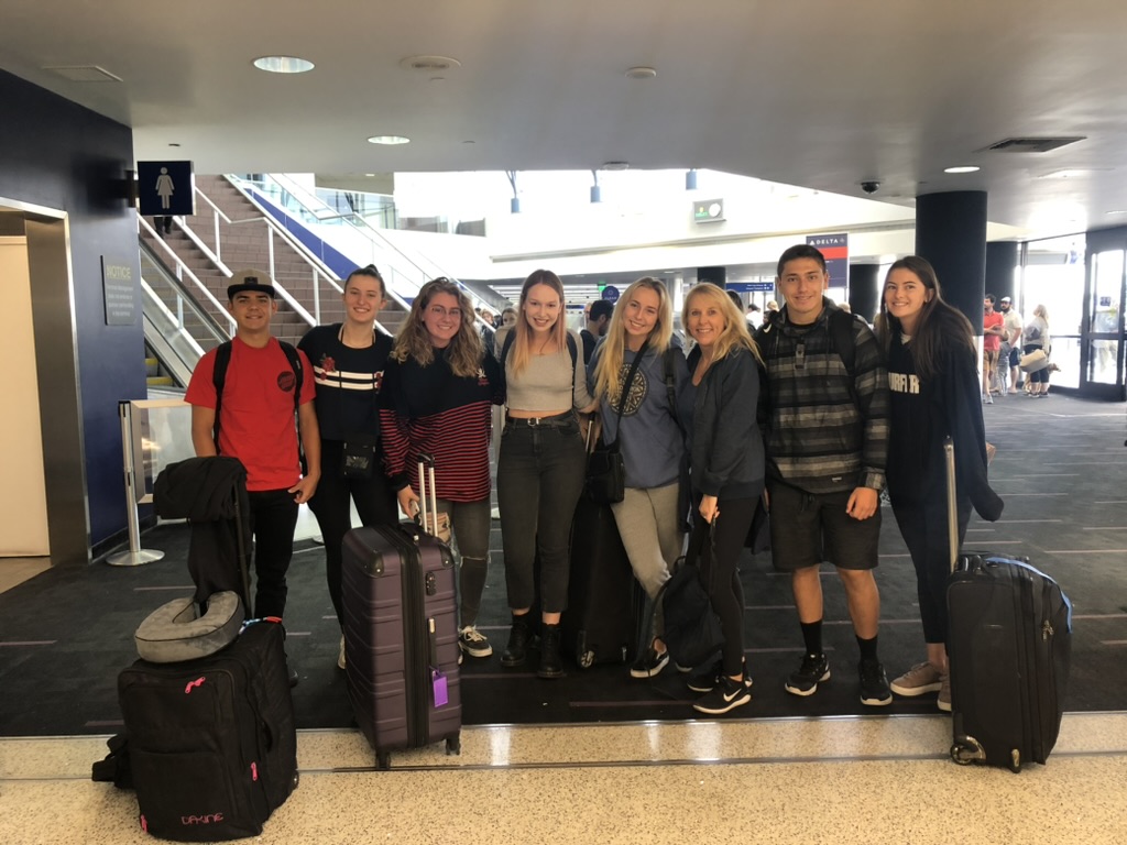 Group of young travelers with luggage smiling at airport terminal before departure.