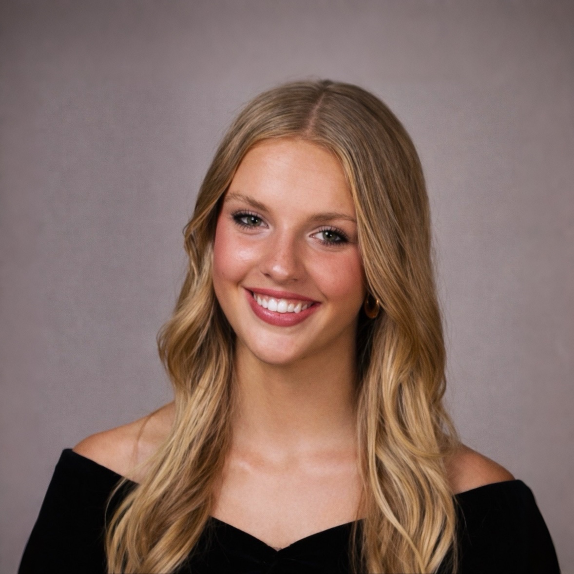 Headshot of a smiling young woman with wavy blonde hair and natural makeup against a neutral background.