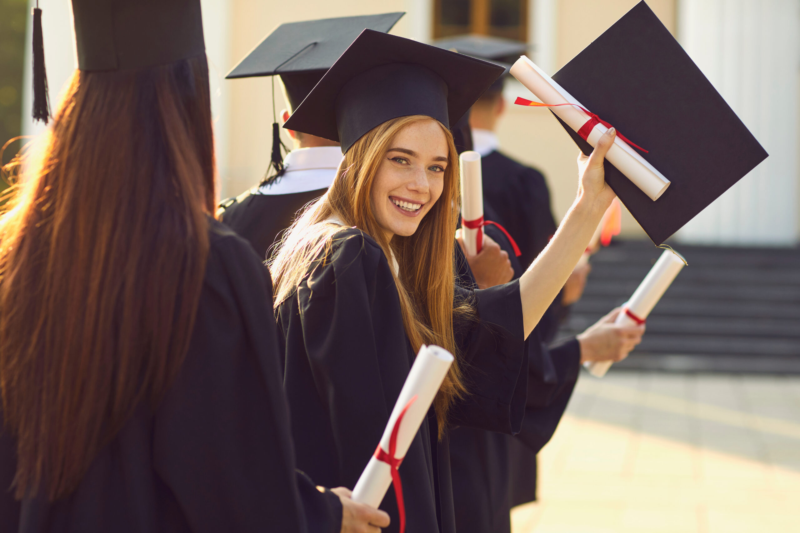 Smiling graduates in caps and gowns holding diplomas during graduation celebration.