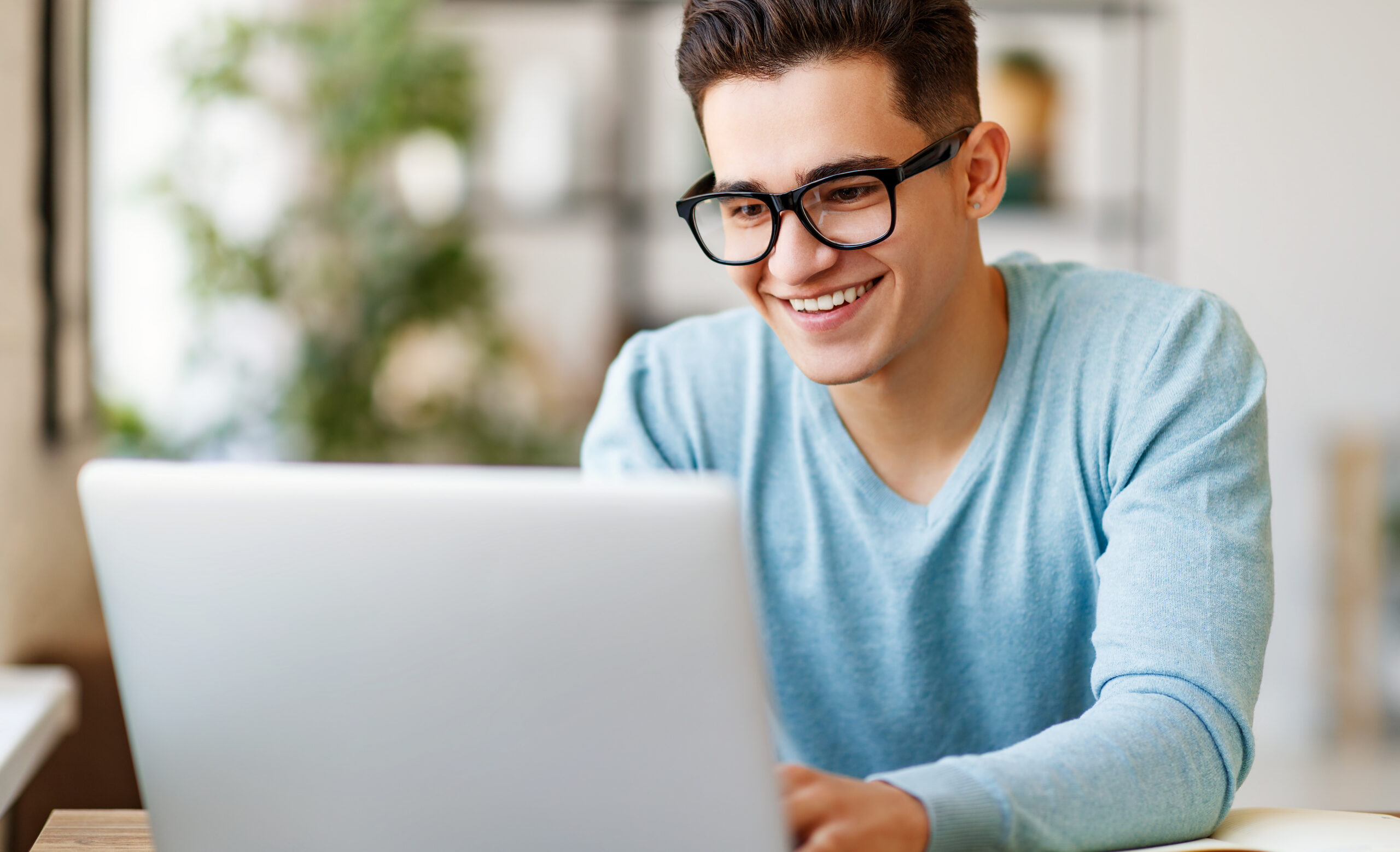 Male student smiling while studying on laptop in bright indoor setting.