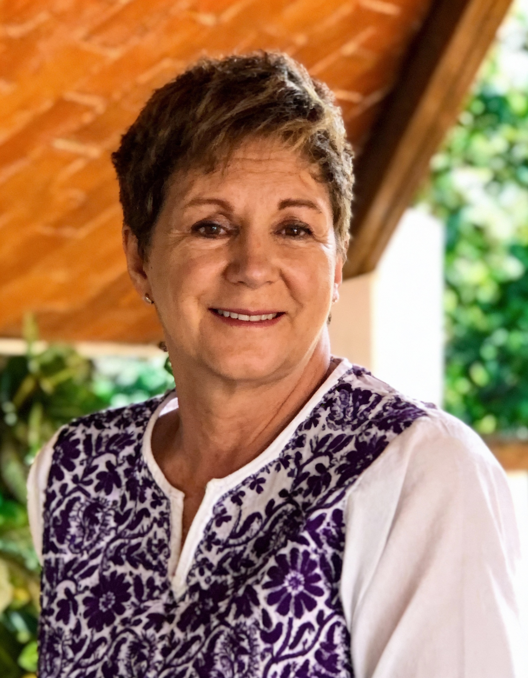 Woman in a patterned vest smiling in a casual outdoor portrait.