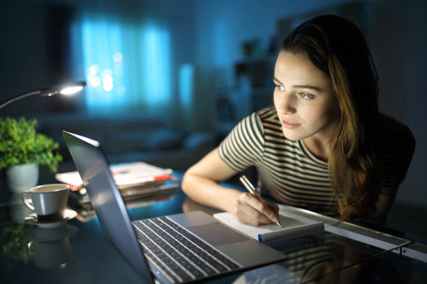Woman writing notes checking laptop content in the night
